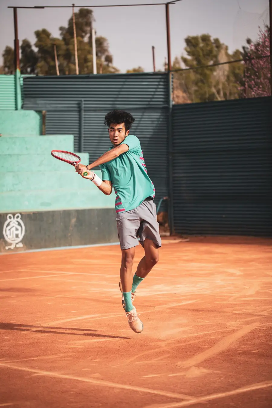 Jovem tenista saltando para um backhand em quadra de saibro